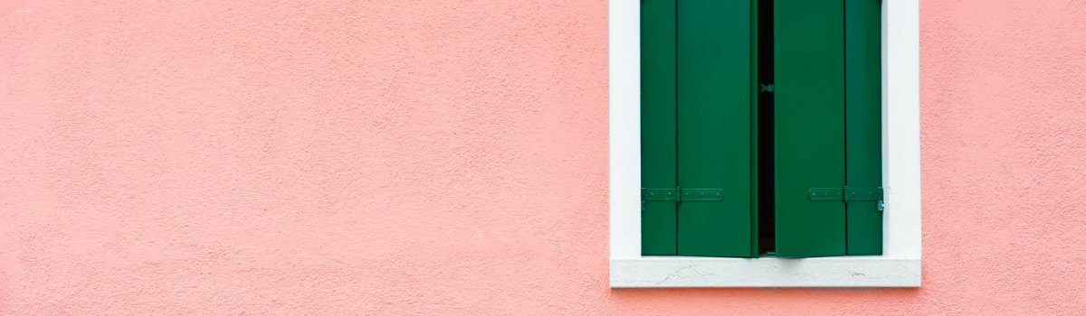 Ein Fenster mit grünen Fensterläden an einer rosa Wand