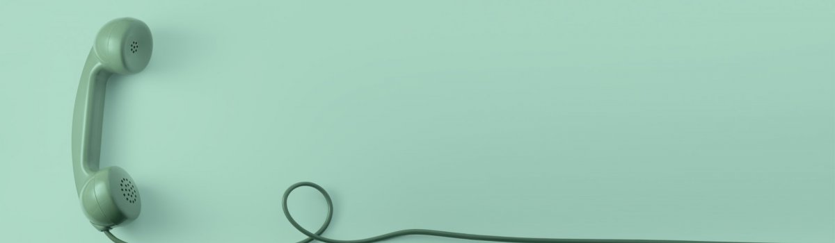 Einen türkisen Telefonhörer mit langer Schnur eines Telefons mit klassischer Wählscheibe vor türkisenem Hintergrund