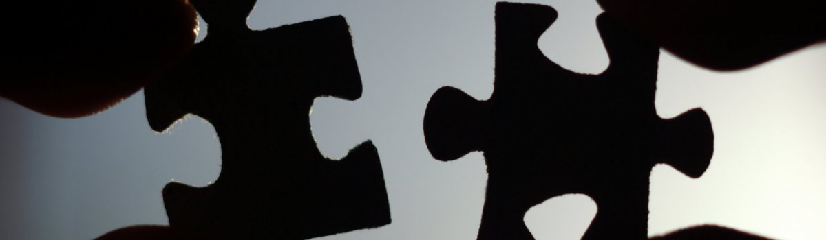 Silhouette von zwei Puzzleteilen, die vor den Himmel gehalten werden.