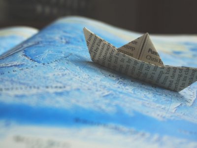 Papierboot auf einem Landkartenbuch.