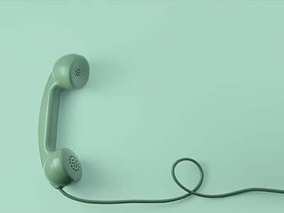 Einen türkisen Telefonhörer mit langer Schnur eines Telefons mit klassischer Wählscheibe vor türkisenem Hintergrund
